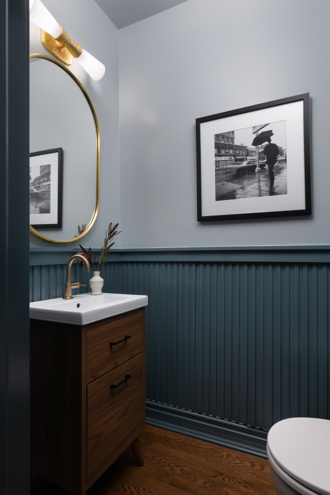 Kleine Moderne Gästetoilette mit verzierten Schränken, hellbraunen Holzschränken, Toilette mit Aufsatzspülkasten, blauer Wandfarbe, braunem Holzboden, integriertem Waschbecken, Quarzwerkstein-Waschtisch, weißer Waschtischplatte, freistehendem Waschtisch und vertäfelten Wänden in Detroit