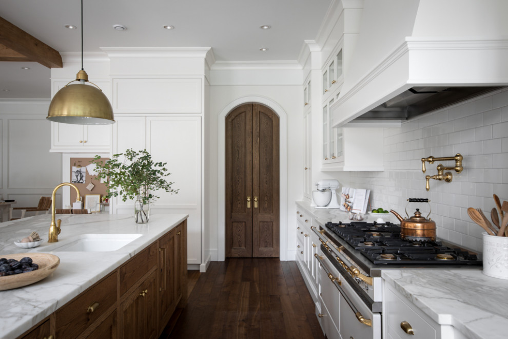 Inspiration for a large transitional u-shaped medium tone wood floor, brown floor and exposed beam open concept kitchen remodel with a farmhouse sink, shaker cabinets, white cabinets, marble countertops, white backsplash, subway tile backsplash, paneled appliances, an island and white countertops
