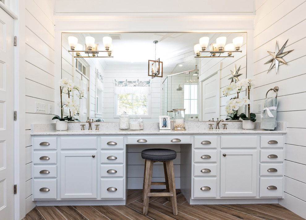 This is an example of a beach style master bathroom in Other with recessed-panel cabinets, white cabinets, a corner shower, white walls, porcelain floors, an undermount sink, brown floor and a hinged shower door.