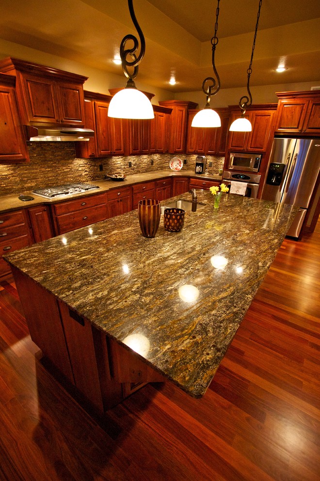 Example of a large l-shaped medium tone wood floor open concept kitchen design with an undermount sink, raised-panel cabinets, dark wood cabinets, multicolored backsplash, glass tile backsplash, stainless steel appliances and an island