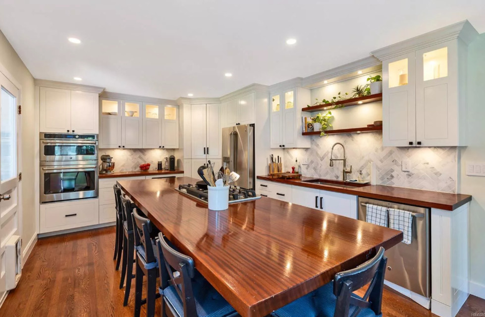 Mid-sized transitional u-shaped dark wood floor and brown floor eat-in kitchen photo in Denver with an undermount sink, recessed-panel cabinets, white cabinets, wood countertops, white backsplash, marble backsplash, stainless steel appliances, an island and brown countertops