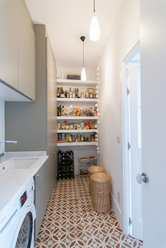 This is an example of a mid-sized transitional single-wall utility room in Madrid with flat-panel cabinets, grey cabinets, marble benchtops, white walls, ceramic floors, a side-by-side washer and dryer and an undermount sink.