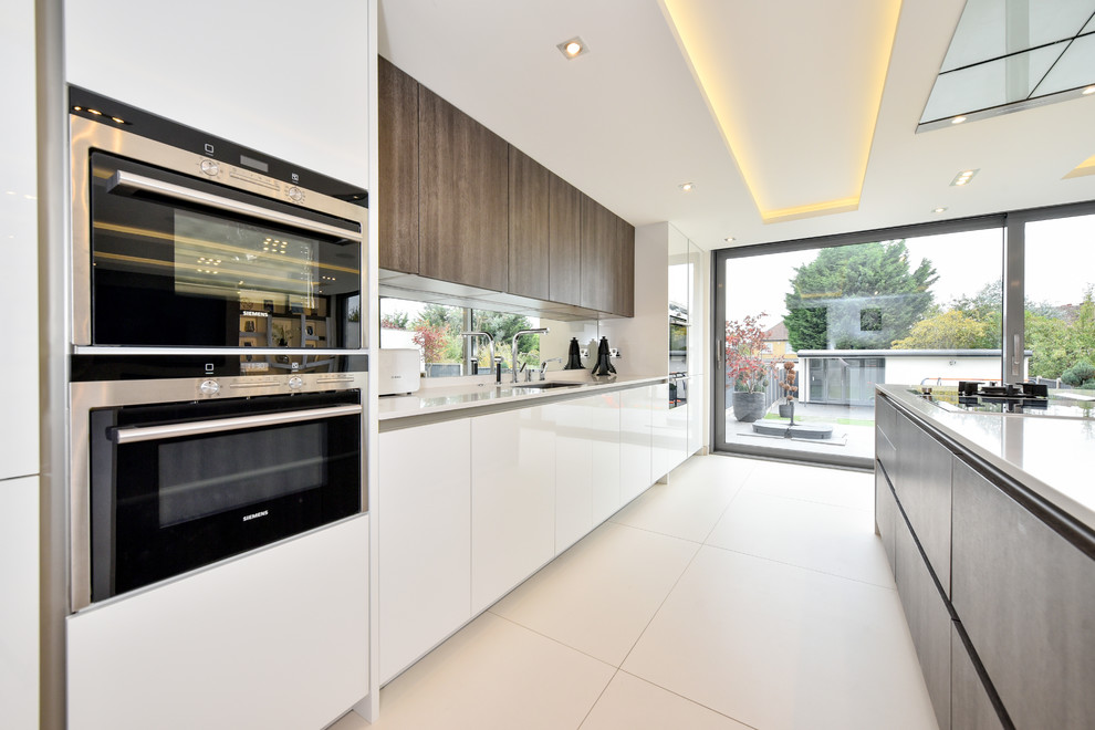 Photo of a mid-sized modern single-wall open plan kitchen in London with a drop-in sink, flat-panel cabinets, white cabinets, quartzite benchtops, metallic splashback, window splashback, black appliances, ceramic floors, with island and white floor.