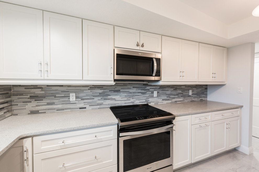 Inspiration for a mid-sized transitional l-shaped porcelain tile and gray floor kitchen pantry remodel in Orlando with an undermount sink, shaker cabinets, white cabinets, quartz countertops, gray backsplash, mosaic tile backsplash, stainless steel appliances, no island and white countertops