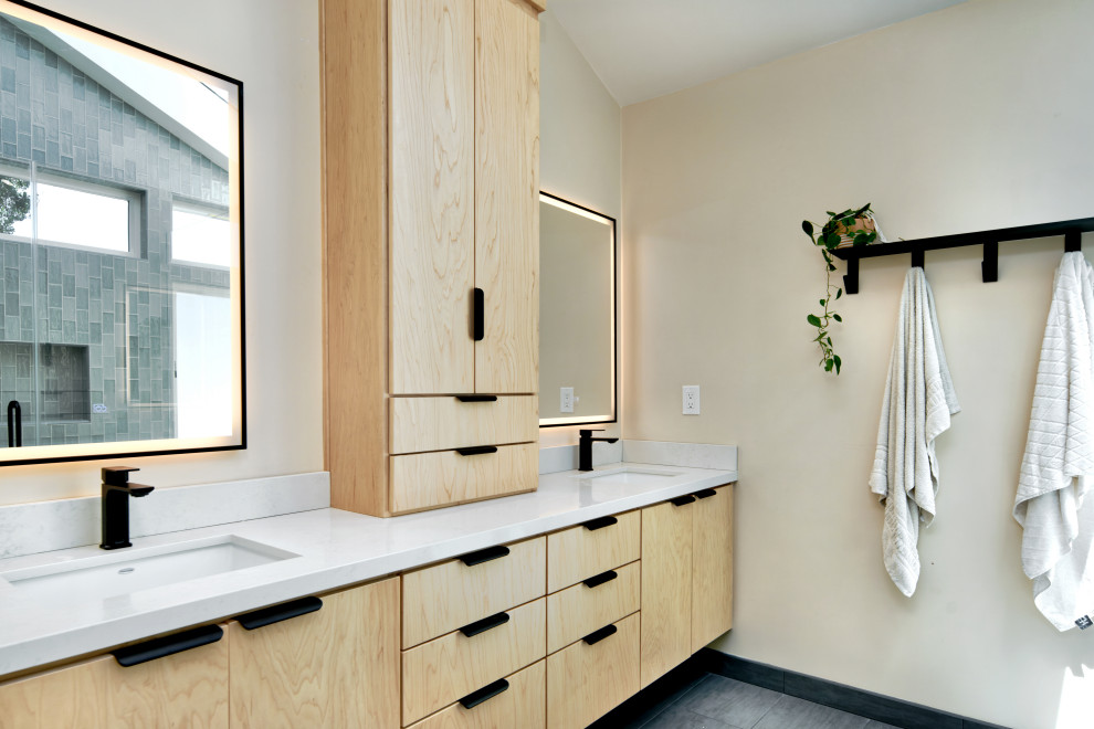 Cette image montre une grande salle de bain design en bois clair avec un placard à porte plane, un mur blanc, un sol en carrelage de porcelaine, un lavabo encastré, un plan de toilette en quartz modifié, un sol gris, un plan de toilette blanc, meuble double vasque et meuble-lavabo encastré.