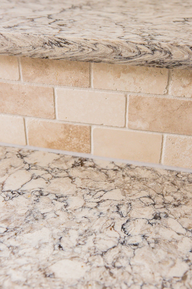 Example of a mid-sized transitional l-shaped medium tone wood floor eat-in kitchen design in Austin with an undermount sink, recessed-panel cabinets, white cabinets, granite countertops, beige backsplash, stone tile backsplash, stainless steel appliances and an island