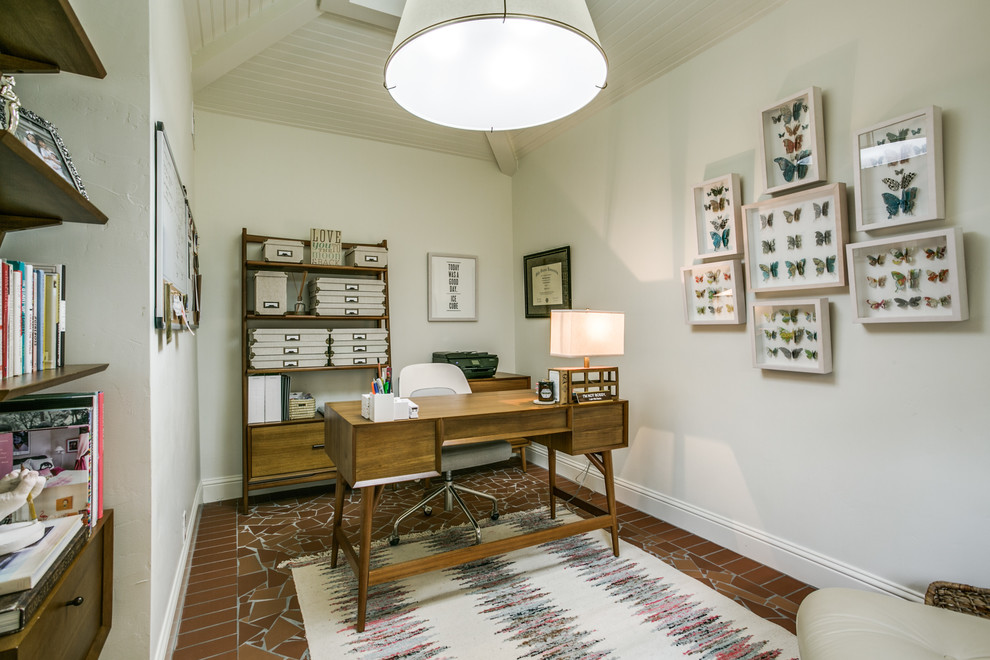 Transitional home office in Dallas with white walls, terra-cotta floors, a freestanding desk and brown floor.
