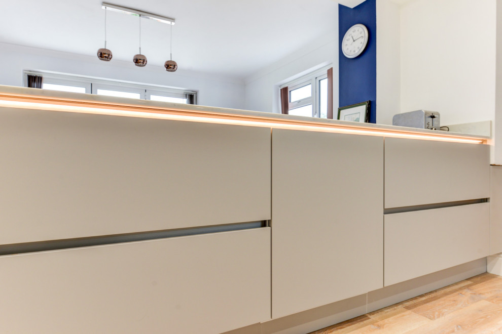Photo of a mid-sized modern single-wall eat-in kitchen in Sussex with an undermount sink, flat-panel cabinets, grey cabinets, quartzite benchtops, blue splashback, glass sheet splashback, panelled appliances, vinyl floors, with island, brown floor and white benchtop.