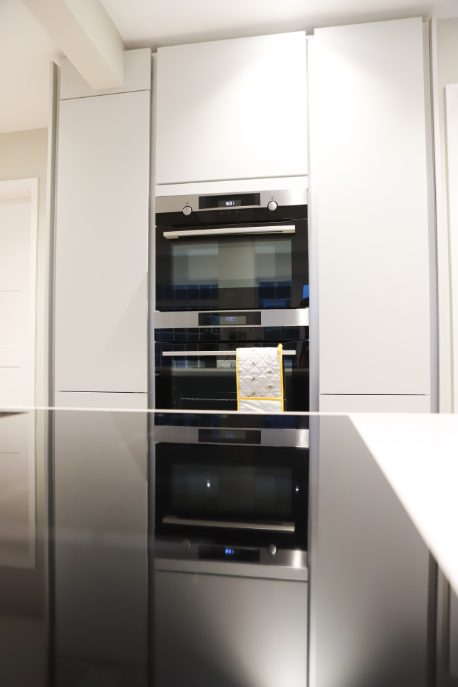 Photo of a medium sized contemporary cream and black open plan kitchen in Essex with an integrated sink, flat-panel cabinets, black cabinets, stainless steel appliances, an island, multi-coloured floors and white worktops.