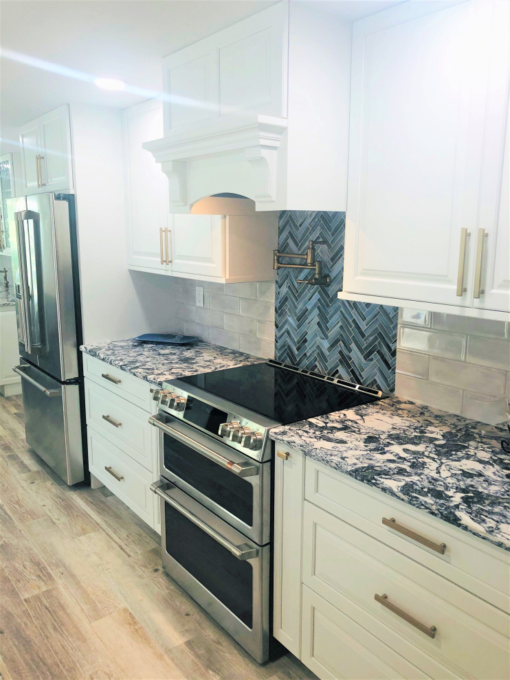 This is an example of a large beach style l-shaped eat-in kitchen in Miami with an undermount sink, raised-panel cabinets, white cabinets, quartz benchtops, multi-coloured splashback, porcelain splashback, stainless steel appliances, porcelain floors, with island, brown floor and multi-coloured benchtop.