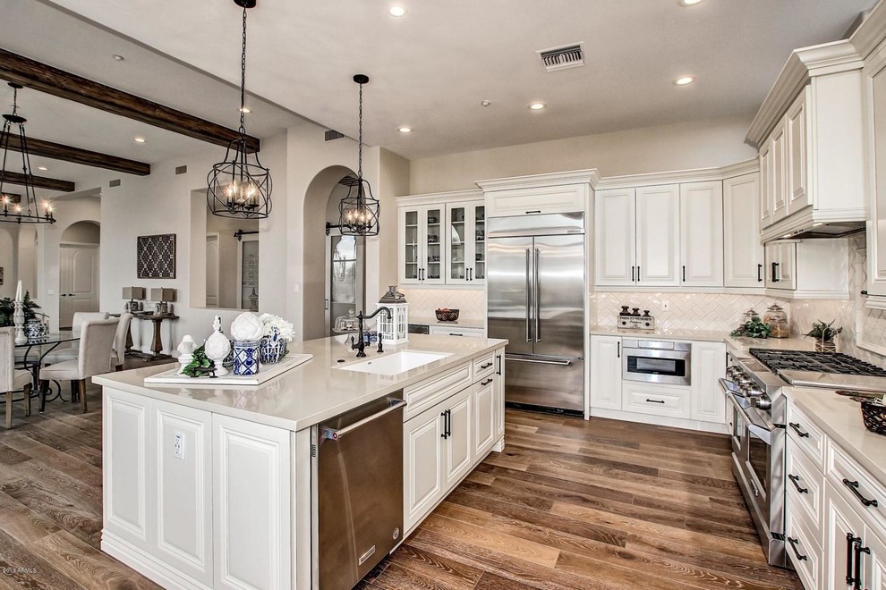 Inspiration for a mid-sized transitional l-shaped open plan kitchen in Phoenix with a single-bowl sink, raised-panel cabinets, white cabinets, quartzite benchtops, beige splashback, ceramic splashback, stainless steel appliances, medium hardwood floors, with island and multi-coloured floor.