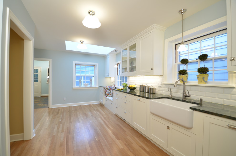 Mid-sized arts and crafts galley eat-in kitchen in Portland with a farmhouse sink, shaker cabinets, white cabinets, granite benchtops, white splashback, ceramic splashback, stainless steel appliances, light hardwood floors and no island.