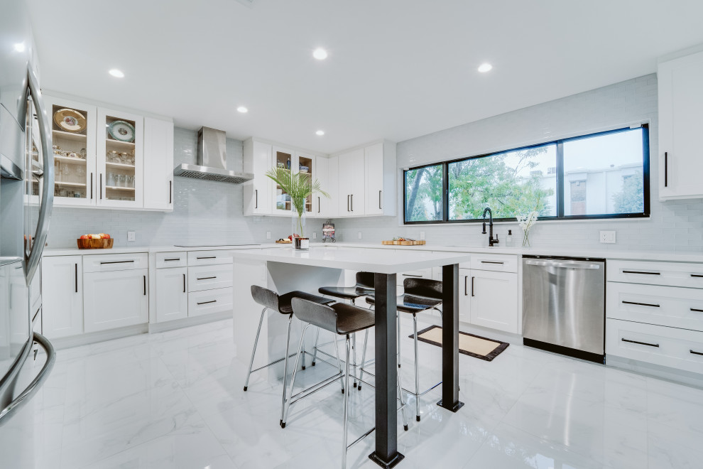 Large contemporary u-shaped eat-in kitchen in Miami with an undermount sink, shaker cabinets, white cabinets, grey splashback, glass tile splashback, stainless steel appliances, ceramic floors, with island, grey floor and white benchtop.