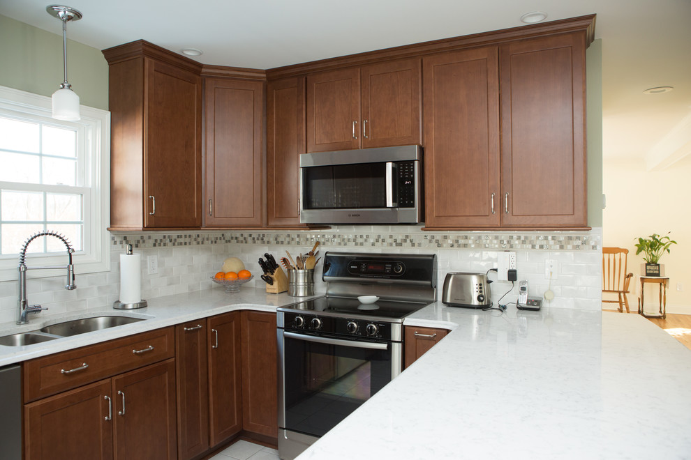 Example of a mid-sized transitional l-shaped white floor and ceramic tile eat-in kitchen design with an undermount sink, quartz countertops, white backsplash, stainless steel appliances, white countertops, shaker cabinets, medium tone wood cabinets, porcelain backsplash and a peninsula