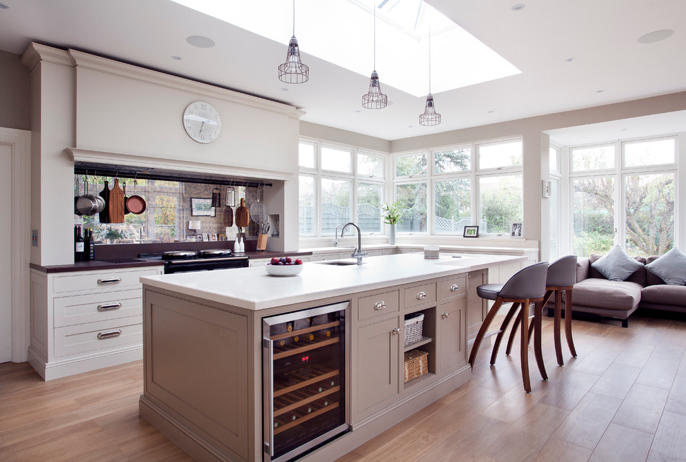 Photo of a country galley open plan kitchen in Dublin with an undermount sink, beaded inset cabinets, white cabinets, metallic splashback, mirror splashback, light hardwood floors, with island and stainless steel appliances.