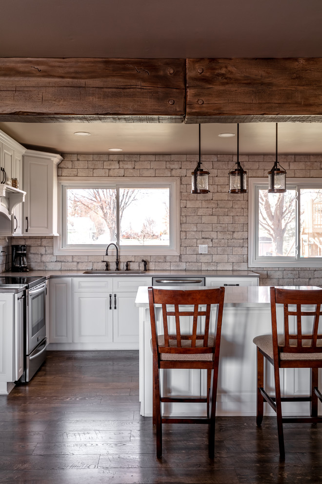 Mid-sized mountain style u-shaped laminate floor and brown floor open concept kitchen photo in Toronto with an undermount sink, raised-panel cabinets, white cabinets, quartzite countertops, white backsplash, brick backsplash, stainless steel appliances, an island and gray countertops