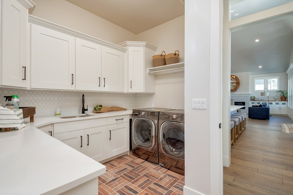Mid-sized contemporary l-shaped utility room in Boise with an undermount sink, shaker cabinets, white cabinets, solid surface benchtops, beige walls, brick floors, a side-by-side washer and dryer, multi-coloured floor and white benchtop.