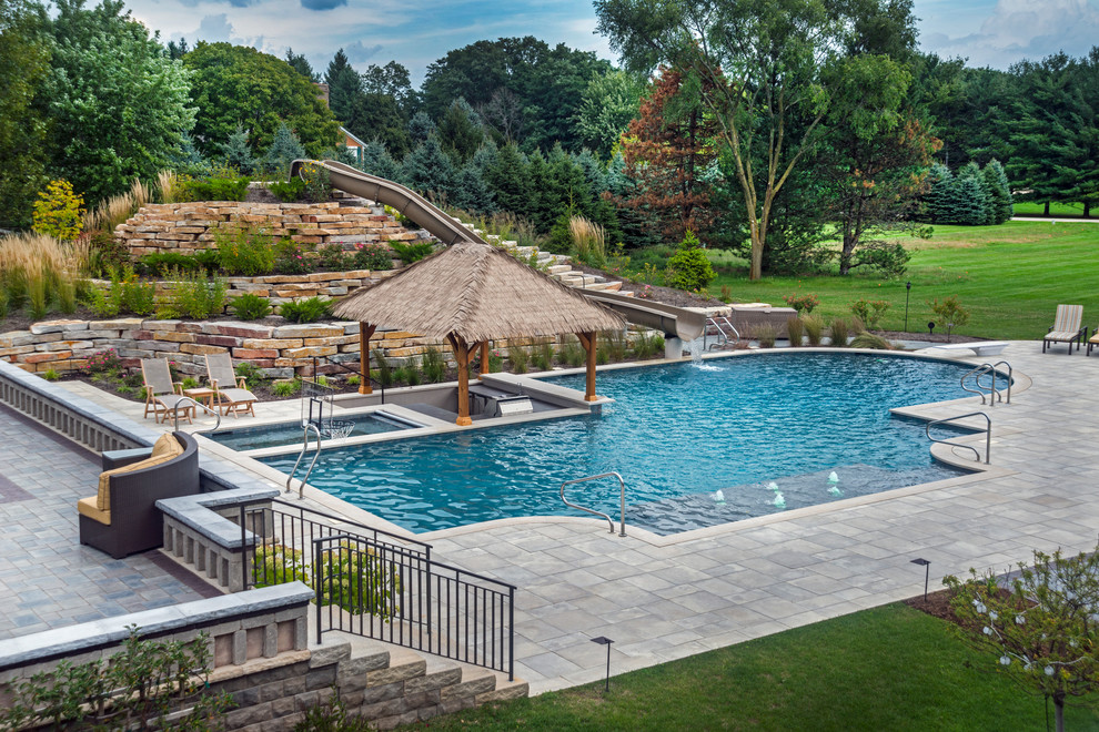 Expansive tropical backyard custom-shaped lap pool in Chicago with a water slide and natural stone pavers.