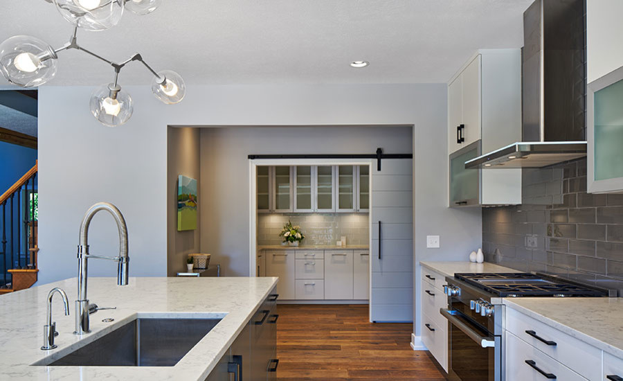 This is an example of a large modern single-wall eat-in kitchen in Grand Rapids with an undermount sink, white cabinets, grey splashback, brick splashback, stainless steel appliances, medium hardwood floors, with island, brown floor and white benchtop.