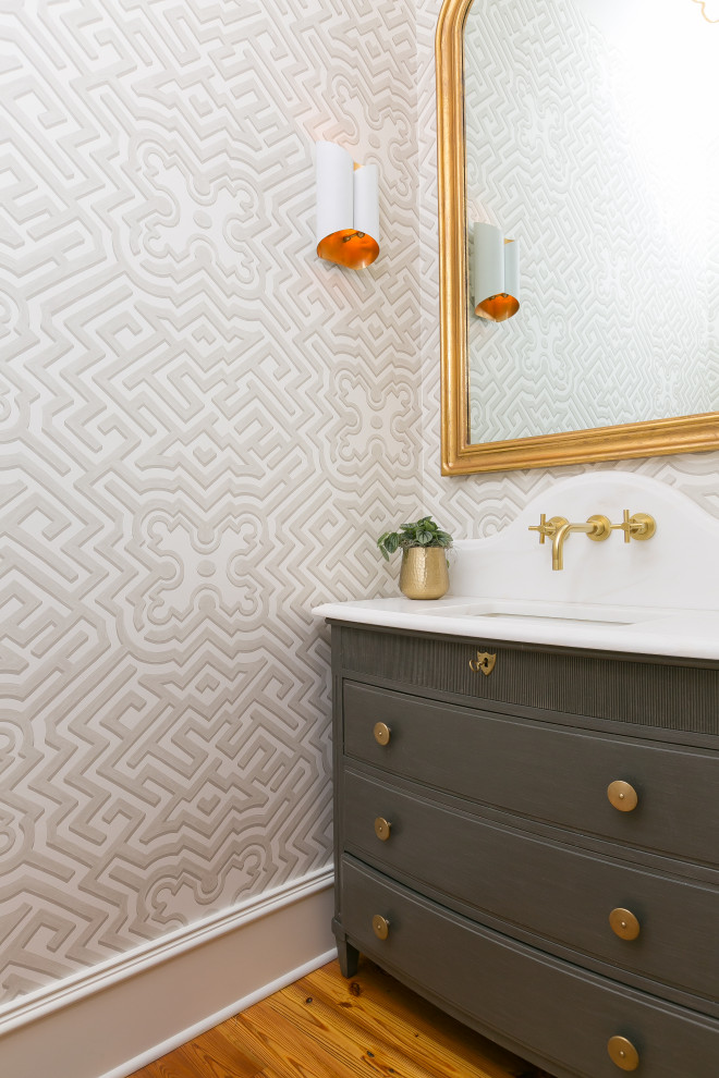 Inspiration for a transitional powder room in Charleston with flat-panel cabinets, grey cabinets, grey walls, medium hardwood floors, an undermount sink, brown floor, white benchtops, a freestanding vanity and wallpaper.