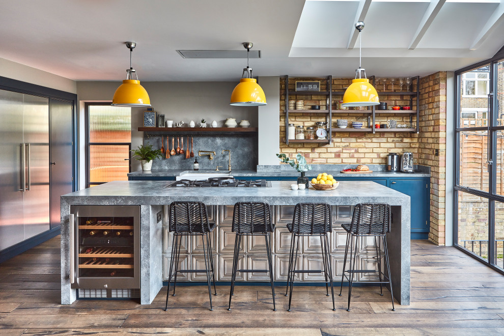 Photo of an industrial galley open plan kitchen in London with an undermount sink, flat-panel cabinets, blue cabinets, grey splashback, dark hardwood floors, with island, brown floor, grey benchtop and vaulted.