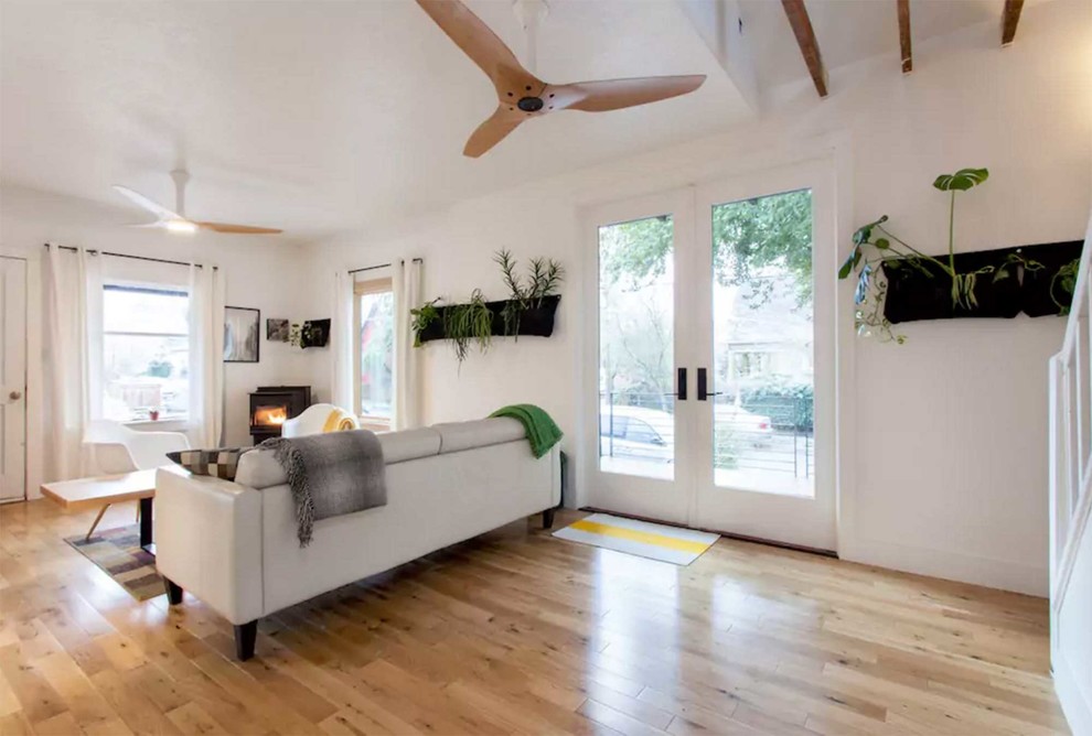 Diseño de salón abierto actual de tamaño medio con paredes blancas, suelo de madera clara, estufa de leña y marco de chimenea de yeso