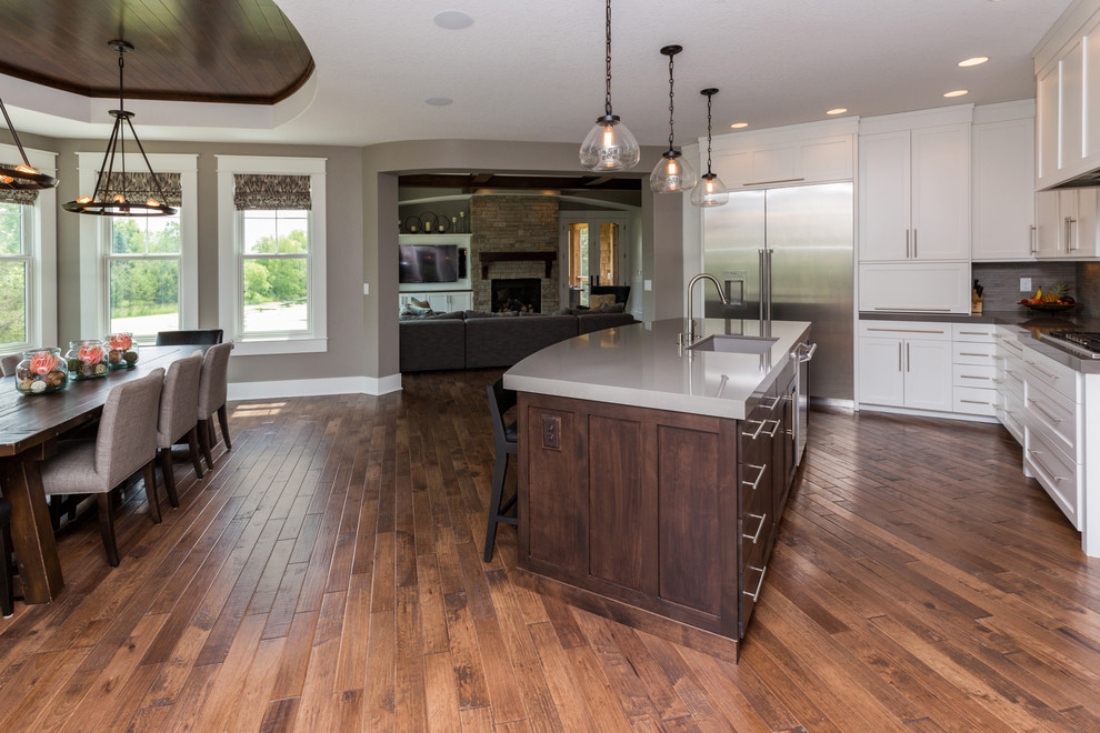 Large transitional l-shaped dark wood floor eat-in kitchen photo with an undermount sink, shaker cabinets, white cabinets, solid surface countertops, gray backsplash, stainless steel appliances and an island