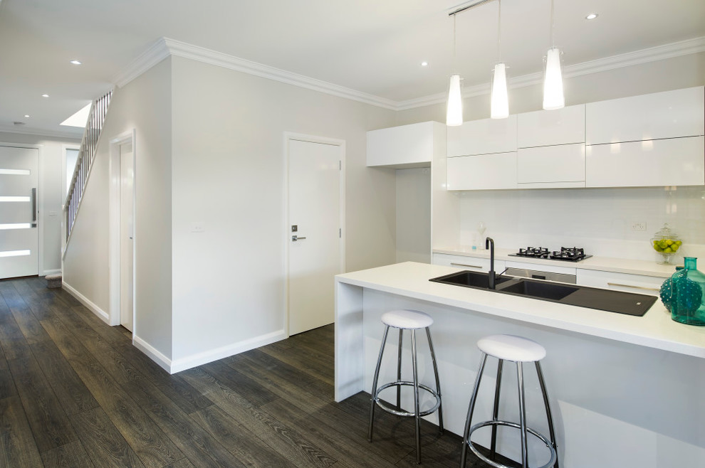 This is an example of a mid-sized contemporary single-wall kitchen pantry in Melbourne with an integrated sink, recessed-panel cabinets, white cabinets, granite benchtops, white splashback, ceramic splashback, stainless steel appliances, dark hardwood floors and with island.