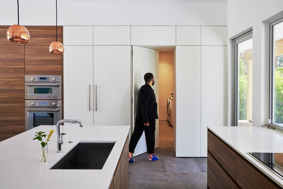 Foto på ett stort funkis vit kök, med en undermonterad diskho, släta luckor, skåp i mellenmörkt trä, bänkskiva i kvarts, vitt stänkskydd, klinkergolv i porslin, en köksö och grått golv
