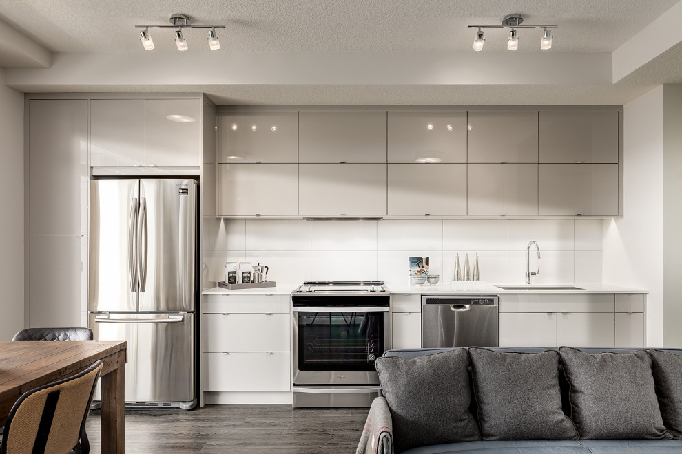 Design ideas for a mid-sized contemporary single-wall eat-in kitchen in Calgary with an undermount sink, flat-panel cabinets, white cabinets, quartz benchtops, white splashback, ceramic splashback, stainless steel appliances, dark hardwood floors, no island, brown floor and white benchtop.