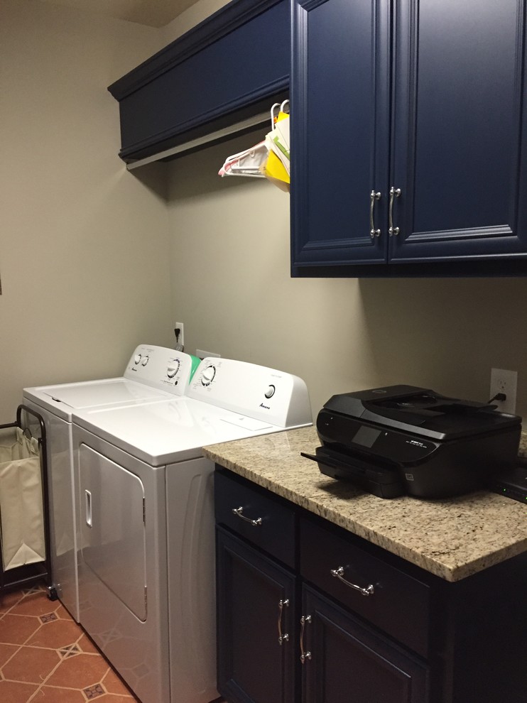 This is an example of a country laundry room in Nashville with raised-panel cabinets, blue cabinets, granite benchtops, grey walls, terra-cotta floors and a side-by-side washer and dryer.