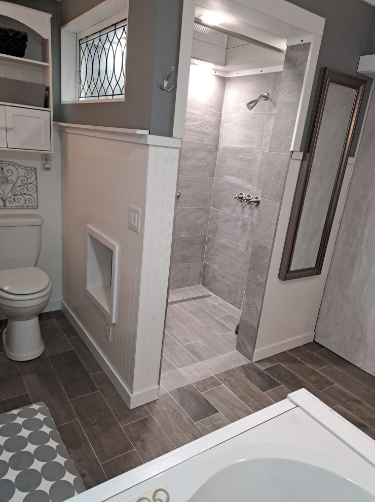 Design ideas for a large master bathroom with flat-panel cabinets, grey cabinets, a curbless shower, a two-piece toilet, gray tile, grey walls, porcelain floors, a vessel sink, glass benchtops, grey floor, an open shower, a single vanity, a freestanding vanity, timber and decorative wall panelling.