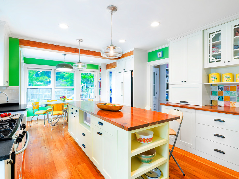 Mid-sized eclectic galley eat-in kitchen in Boston with a farmhouse sink, shaker cabinets, yellow cabinets, wood benchtops, multi-coloured splashback, ceramic splashback, panelled appliances, light hardwood floors and with island.