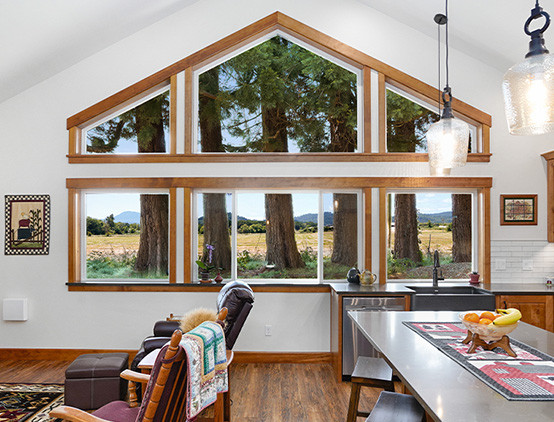 Example of a large mountain style medium tone wood floor, brown floor and vaulted ceiling kitchen design with a farmhouse sink, raised-panel cabinets, medium tone wood cabinets, concrete countertops, white backsplash, ceramic backsplash, stainless steel appliances, an island and gray countertops