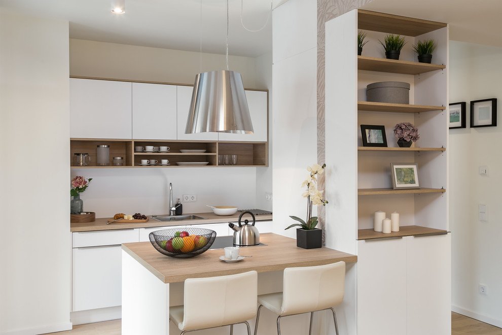 Inspiration for a small contemporary galley eat-in kitchen in Berlin with a single-bowl sink, flat-panel cabinets, white cabinets, wood benchtops, white splashback, light hardwood floors, a peninsula, brown floor and brown benchtop.
