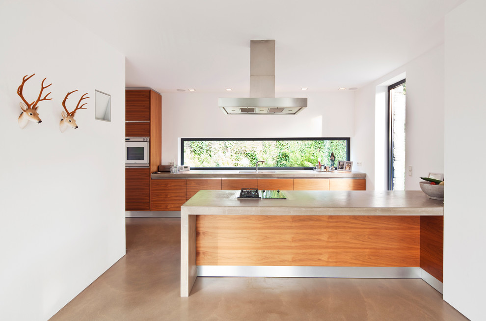 Photo of a mid-sized modern open plan kitchen in Bonn with flat-panel cabinets, medium wood cabinets, concrete benchtops, concrete floors, a peninsula, a drop-in sink and panelled appliances.