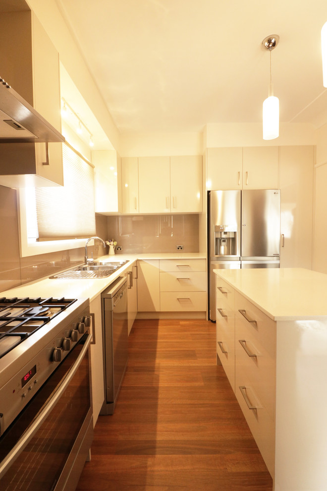 Photo of a mid-sized contemporary u-shaped kitchen pantry in Sydney with a drop-in sink, flat-panel cabinets, beige cabinets, quartz benchtops, brown splashback, glass sheet splashback, stainless steel appliances, light hardwood floors, with island and yellow floor.