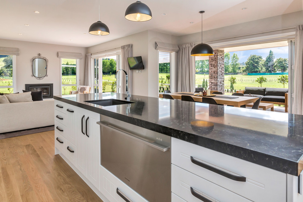 Large contemporary galley eat-in kitchen in Hamilton with an undermount sink, white cabinets, white splashback, glass sheet splashback, stainless steel appliances, light hardwood floors and with island.
