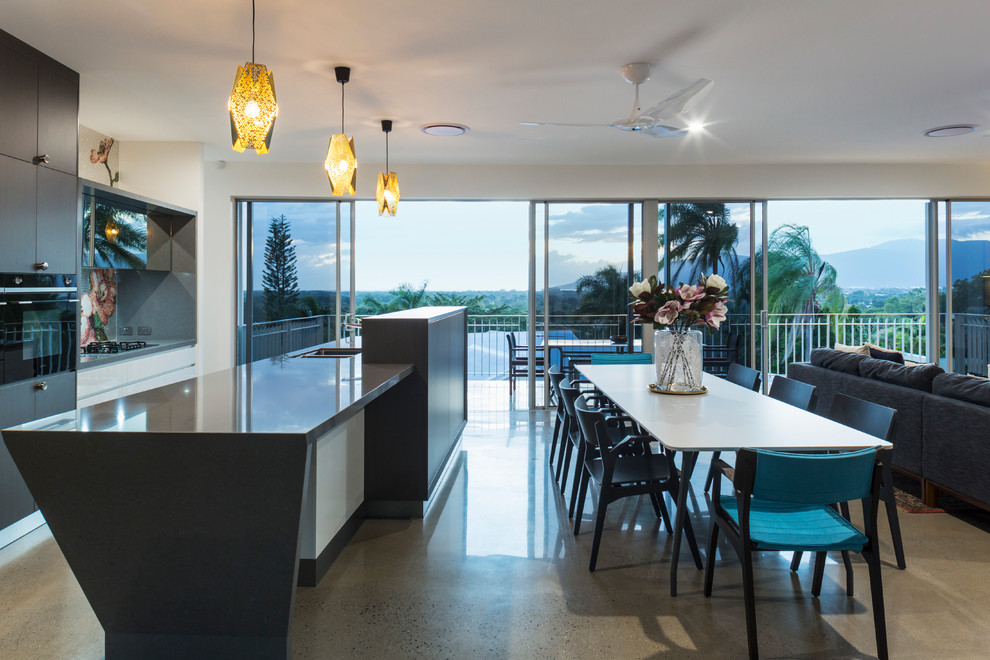This is an example of a galley open plan kitchen in Cairns with concrete floors, dark wood cabinets, solid surface benchtops, with island, grey floor, grey benchtop, mosaic tile splashback and black appliances.
