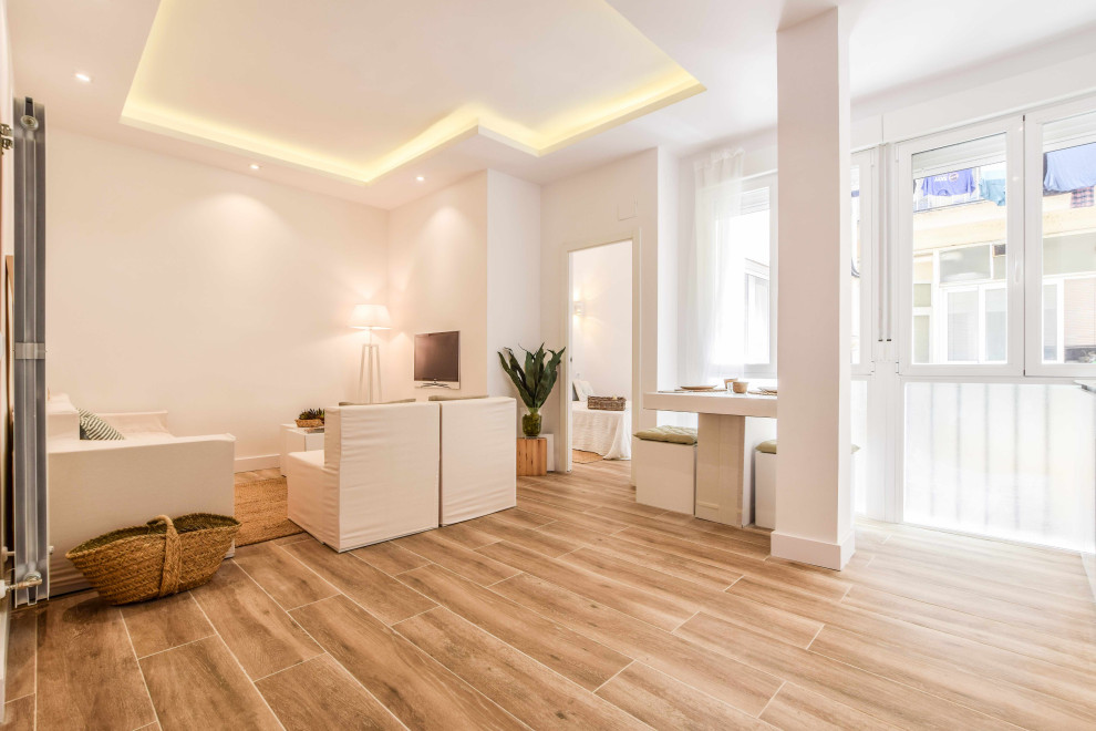 Modelo de sala de estar abierta mediterránea de tamaño medio con paredes blancas, suelo de baldosas de porcelana, televisor colgado en la pared, suelo marrón y casetón
