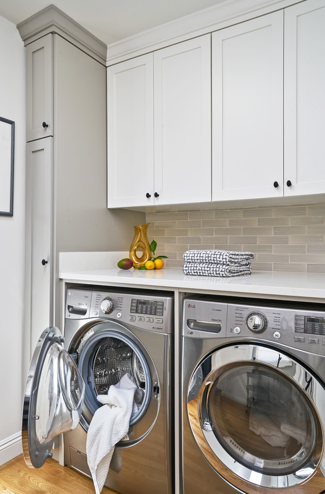 Transitional laundry room in Los Angeles with shaker cabinets, white cabinets, quartz benchtops, a side-by-side washer and dryer, white benchtop, medium hardwood floors and brown floor.