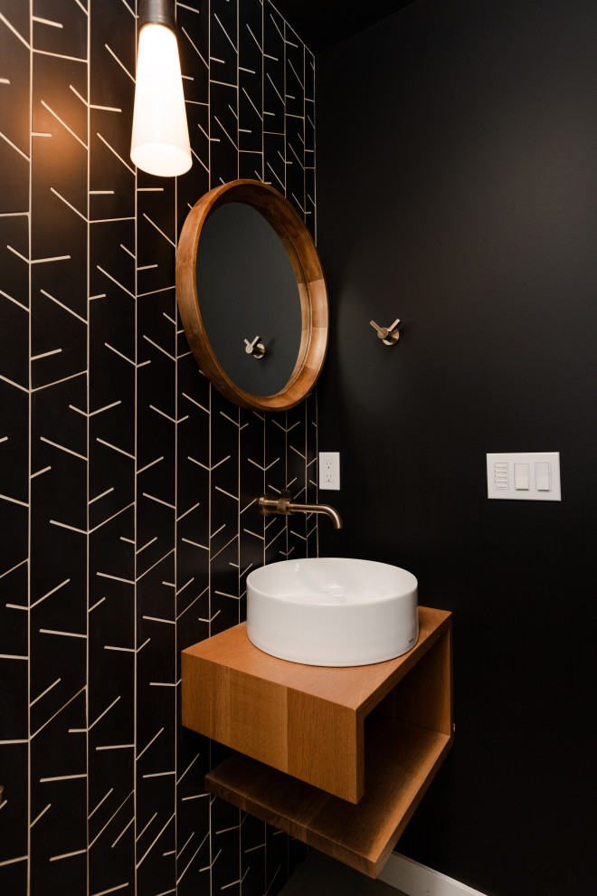 Aménagement d'un petit WC et toilettes rétro en bois brun avec un placard sans porte, WC à poser, un carrelage noir, des carreaux de porcelaine, un mur noir, sol en béton ciré, une vasque, un sol gris et meuble-lavabo suspendu.