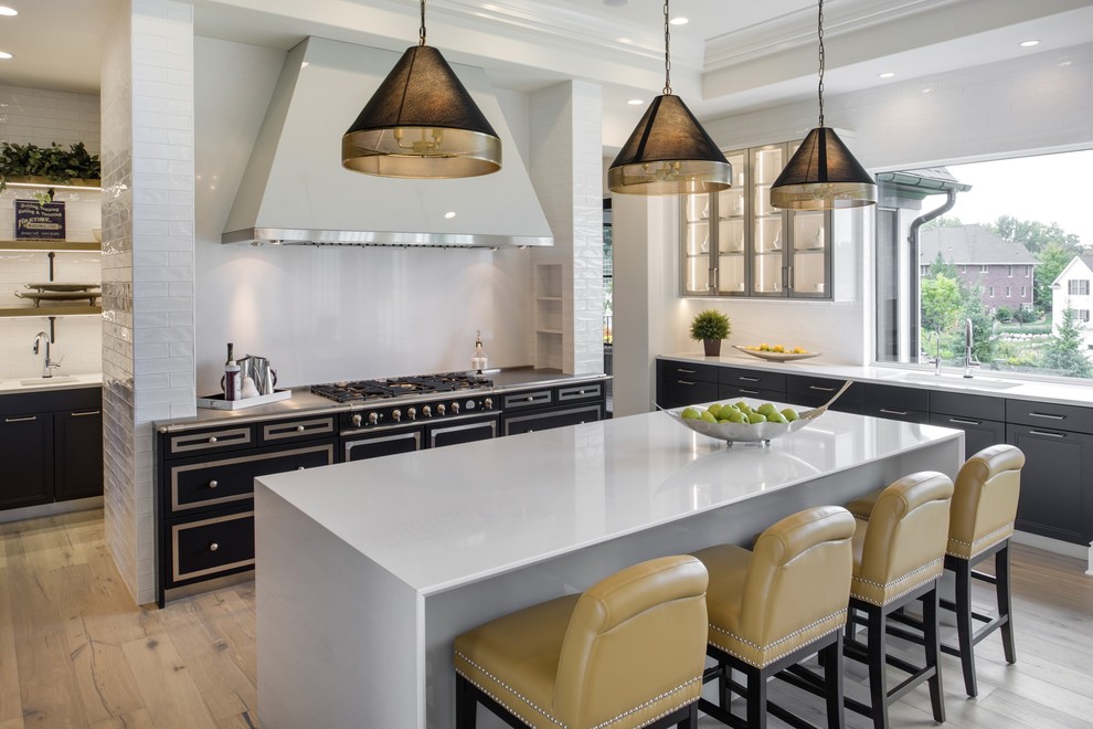Photo of a transitional kitchen in Minneapolis with a single-bowl sink, beaded inset cabinets, black cabinets, white splashback, glass sheet splashback, black appliances, light hardwood floors and with island.