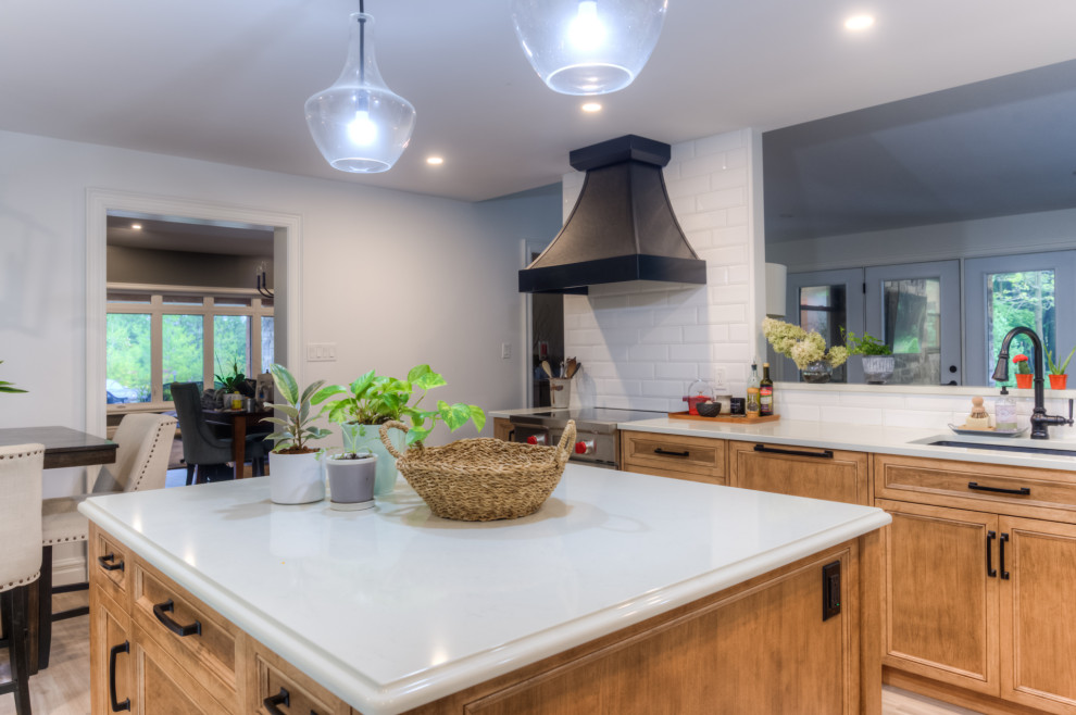 Inspiration for a transitional l-shaped kitchen remodel in Toronto with an undermount sink, shaker cabinets, light wood cabinets, white backsplash, stainless steel appliances, an island and white countertops