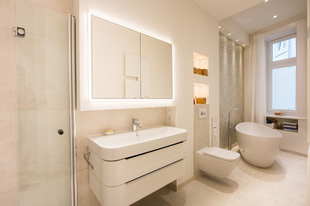 Design ideas for a mid-sized contemporary 3/4 bathroom in Hamburg with flat-panel cabinets, white cabinets, a freestanding tub, a wall-mount toilet, an integrated sink, beige tile, cement tile, beige walls, cement tiles, solid surface benchtops and beige floor.