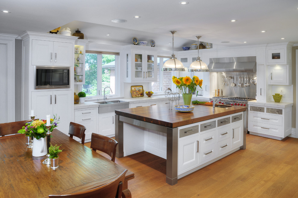 Photo of an expansive traditional u-shaped eat-in kitchen in Toronto with stainless steel appliances, wood benchtops, a farmhouse sink, recessed-panel cabinets, white cabinets, metallic splashback, metal splashback, medium hardwood floors and with island.