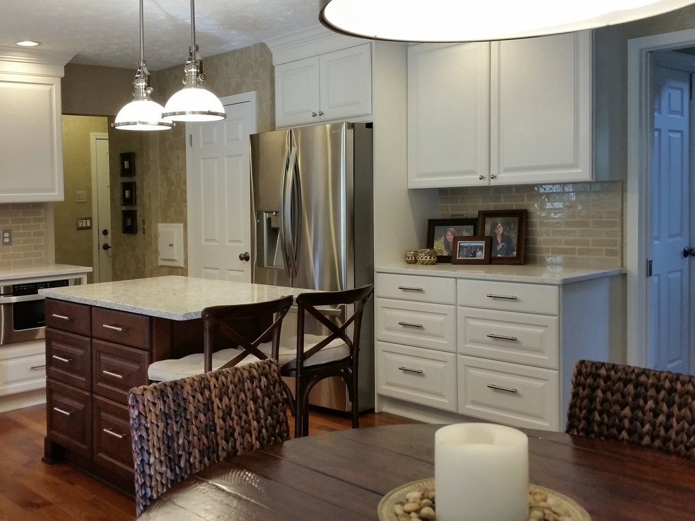 Mid-sized transitional l-shaped medium tone wood floor and brown floor eat-in kitchen photo with raised-panel cabinets, white cabinets, quartz countertops, beige backsplash, subway tile backsplash, stainless steel appliances, an island and white countertops