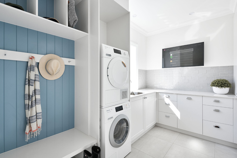 Large beach style l-shaped utility room in Brisbane with an undermount sink, flat-panel cabinets, white cabinets, white walls, a stacked washer and dryer, grey floor and white benchtop.