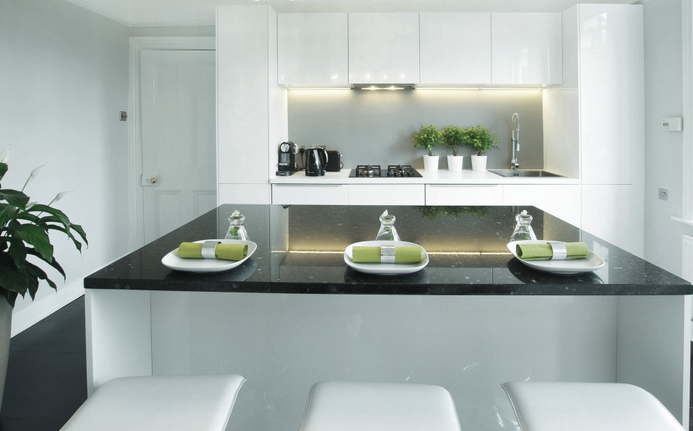 Photo of a mid-sized modern single-wall separate kitchen in London with a single-bowl sink, flat-panel cabinets, white cabinets, granite benchtops, grey splashback, glass tile splashback, black appliances, dark hardwood floors, with island, black floor and black benchtop.