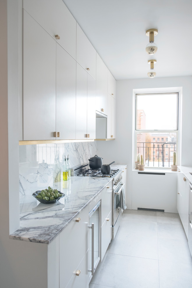 Photo of a mid-sized contemporary galley open plan kitchen in New York with a double-bowl sink, flat-panel cabinets, white cabinets, marble benchtops, white splashback, marble splashback, stainless steel appliances, porcelain floors, no island and grey floor.